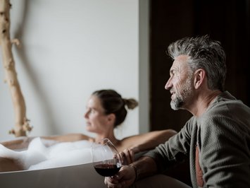 Kessler’s Mountain Lodge: premi Uomo con bicchiere di vino rosso accanto a donna in vasca da bagno schiumata