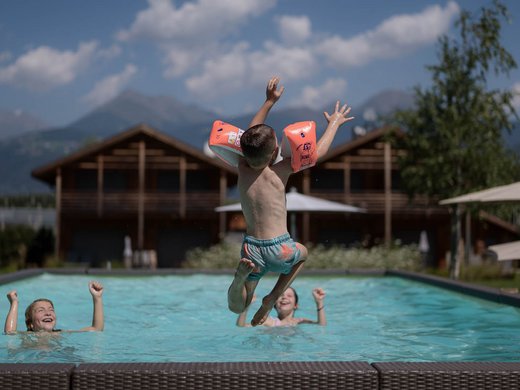 Für Familien Kind mit Schwimmflügeln springt in Pool, zwei Kinder im Wasser, Bergkulisse
