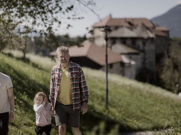 Für Familien Tre persone passeggiano su un sentiero con castello e montagne sullo sfondo