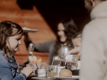 Für Familien Bambina seduta al tavolo mentre qualcuno versa una bevanda in un bicchiere