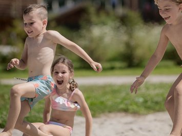 Für Familien Drei Kinder springen und spielen im Sand vor Holzhütten im Sommer
