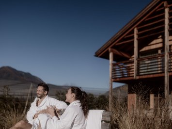 Kessler’s Mountain Lodge: premi Coppia in accappatoi rilassata davanti a una casa in legno sulle montagne