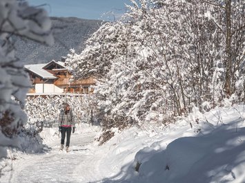 Agriturismo a Bressanone: vacanze invernali Donna che cammina su sentiero innevato con case e montagne sullo sfondo