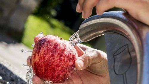 “Premium Terrasse” apartment Hand washing a red apple under running water from a drinking fountain
