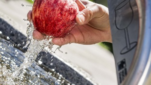 Mit den Öffis ins Chalet Hand wäscht roten Apfel unter fließendem Wasser aus Trinkbrunnen