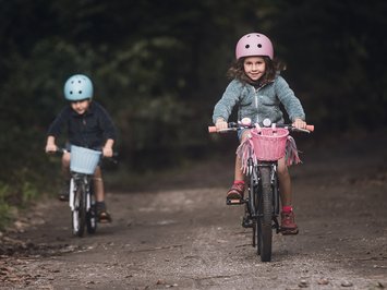 Für Familien Due bambini con caschi in bicicletta su un sentiero nel bosco