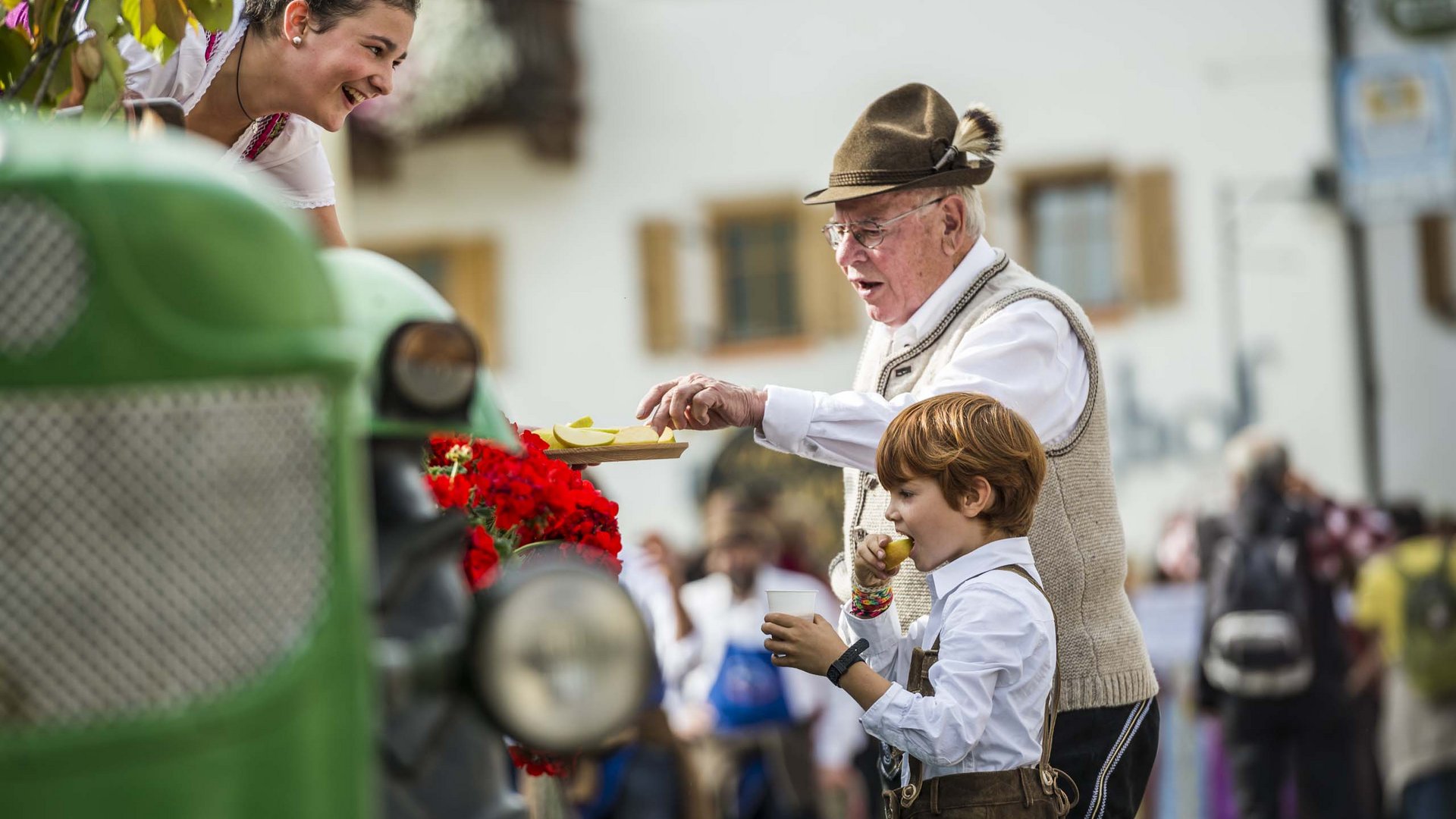 Urlaub nahe Brixen voller Überraschungen Älterer Mann und Kind in Tracht genießen Apfelstücke auf einem Fest