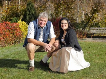 The hosts of your chalets near Brixen Man and woman in traditional clothes sitting on grass in garden in autumn.