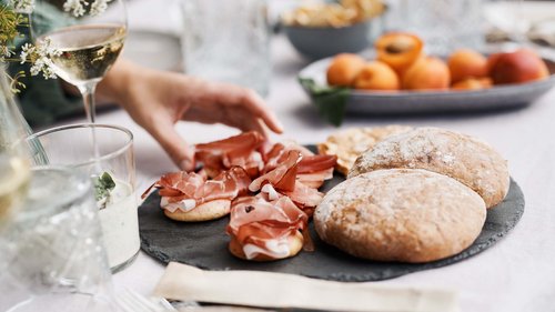 “Premium Terrasse” apartment Hand picking prosciutto on thin bread with rolls and wine on set table