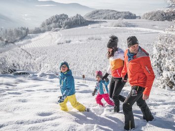 Agriturismo a Bressanone: vacanze invernali Famiglia cammina nella neve in una giornata invernale soleggiata su una collina