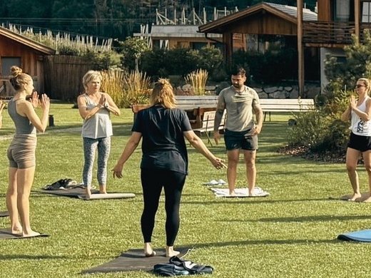 Für Familien Gruppo fa yoga all'aperto su prato verde davanti a case di legno e montagne
