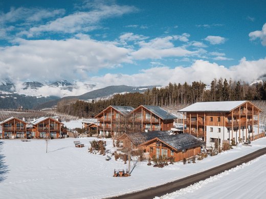 Deine Ferienwohnung in Natz-Schabs: Kessler’s! Holzhäuser im verschneiten Tal mit Bergen und blauem Himmel im Hintergrund