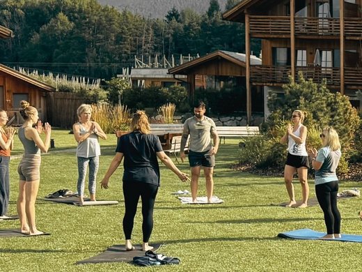 Chalet con sauna privata cercasi? Persone che praticano yoga all'aperto davanti a una casa di legno in montagna