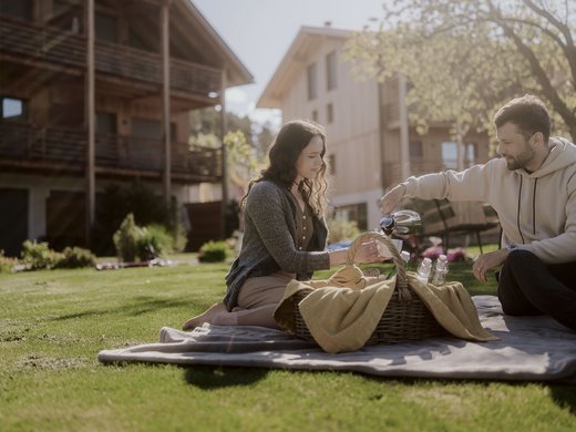 Chalet with a sauna and so much more: Kessler’s Couple having a picnic in the garden in front of wooden houses on a sunny day
