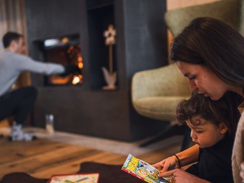 Für Familien Donna legge un libro a un bambino mentre un uomo accende il camino