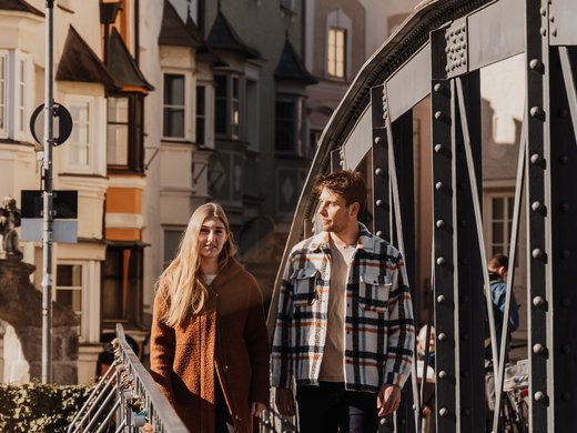 Experience more on your holiday: Explore the charm of South Tyrolean towns while still enjoying the calm and serenity of the mountains. Young couple walking on a city bridge wearing autumn coats