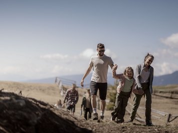 Holiday with a dog in South Tyrol: Kessler’s! Family hiking together on a mountain under a clear blue sky