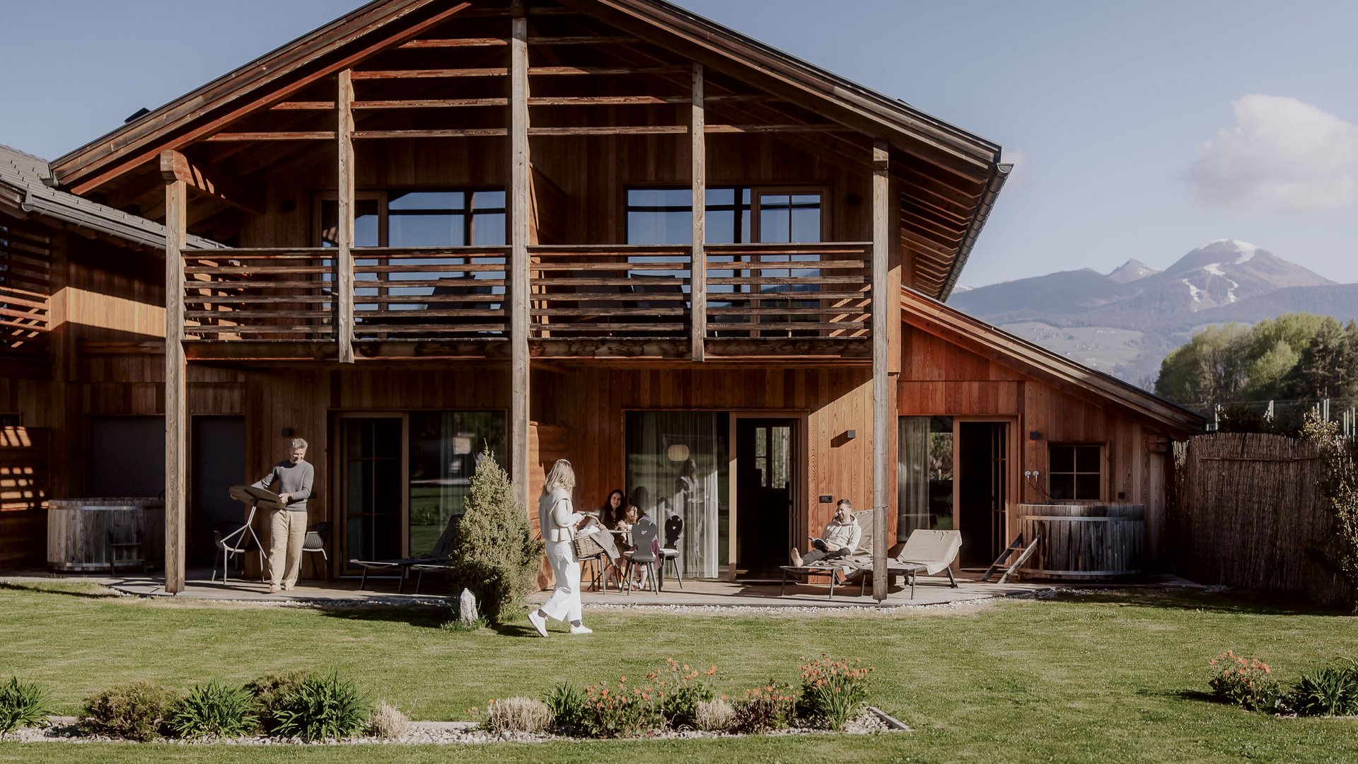 Ferienwohnung in Natz mit dem gewissen Etwas Holzhaus mit Balkon und Menschen im Garten vor Bergkulisse