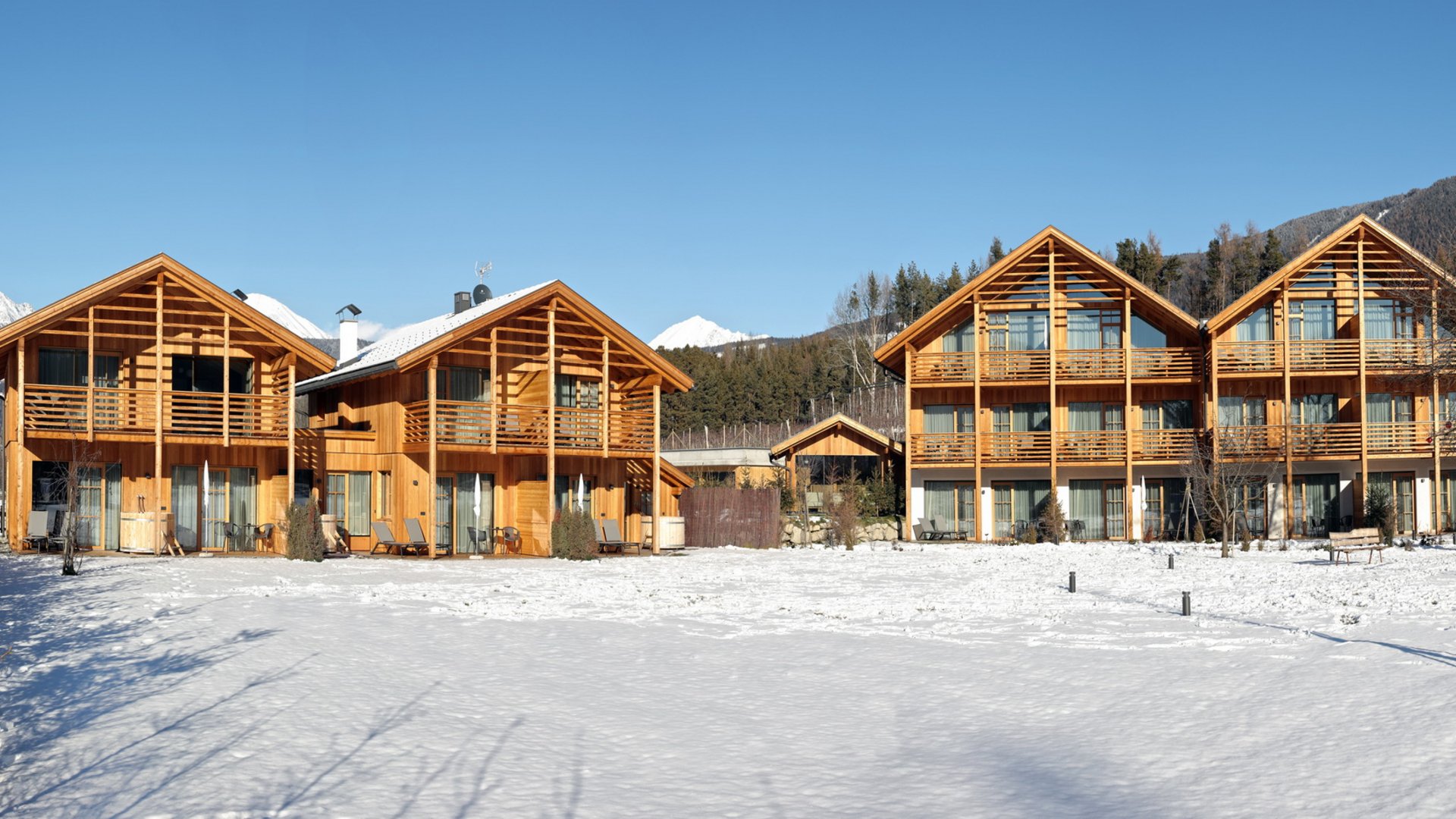 Ferienwohnung in Natz mit dem gewissen Etwas Holzhäuser mit Schnee im Garten und Bergblick bei klarem Himmel