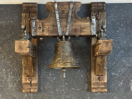 Historische Glocke Alte Bronzeglocke in einem rustikalen Holzgestell an einer dunklen Wand