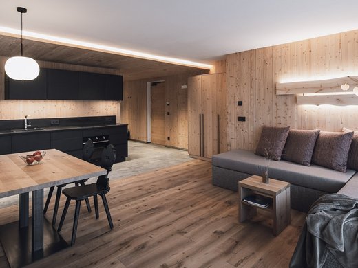 Ferienwohnung in Natz mit dem gewissen Etwas Moderne Wohnküche mit Holzwänden, schwarzer Küchenzeile und grauem Sofa