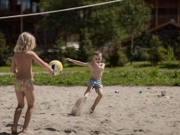 Für Familien Kinder spielen Volleyball im Sand vor Holzhäusern an einem sonnigen Tag