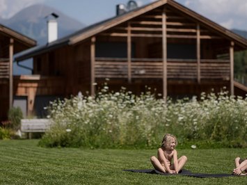 Für Familien Zwei Kinder sitzen auf einer Matte auf dem Gras vor Holzhäusern