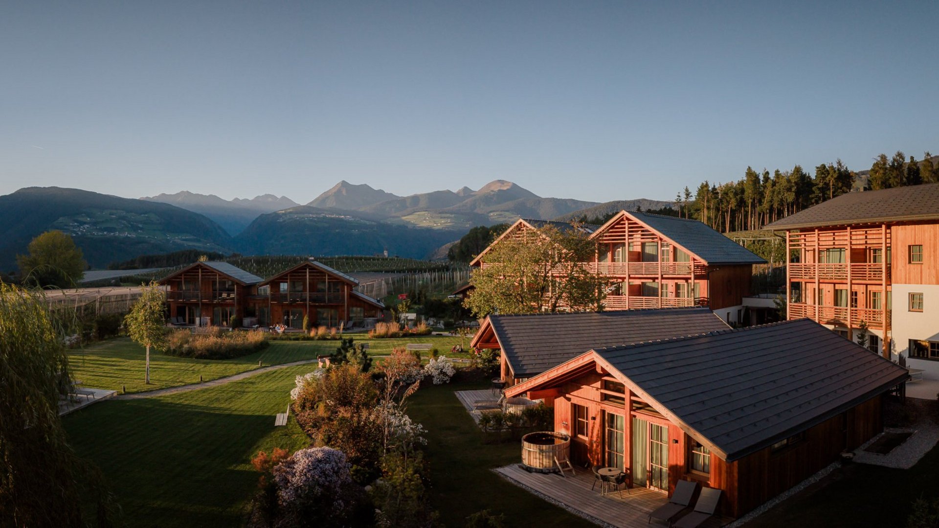 Urlaub in Natz-Schabs? Kessler’s Mountain Lodge! Holzchalets mit gepflegtem Garten vor einer Bergkulisse im Abendlicht