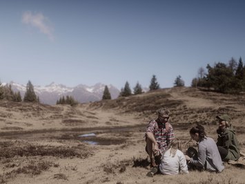 Holiday with a dog in South Tyrol: Kessler’s! Family having a picnic in the mountains with pine trees and clear blue sky