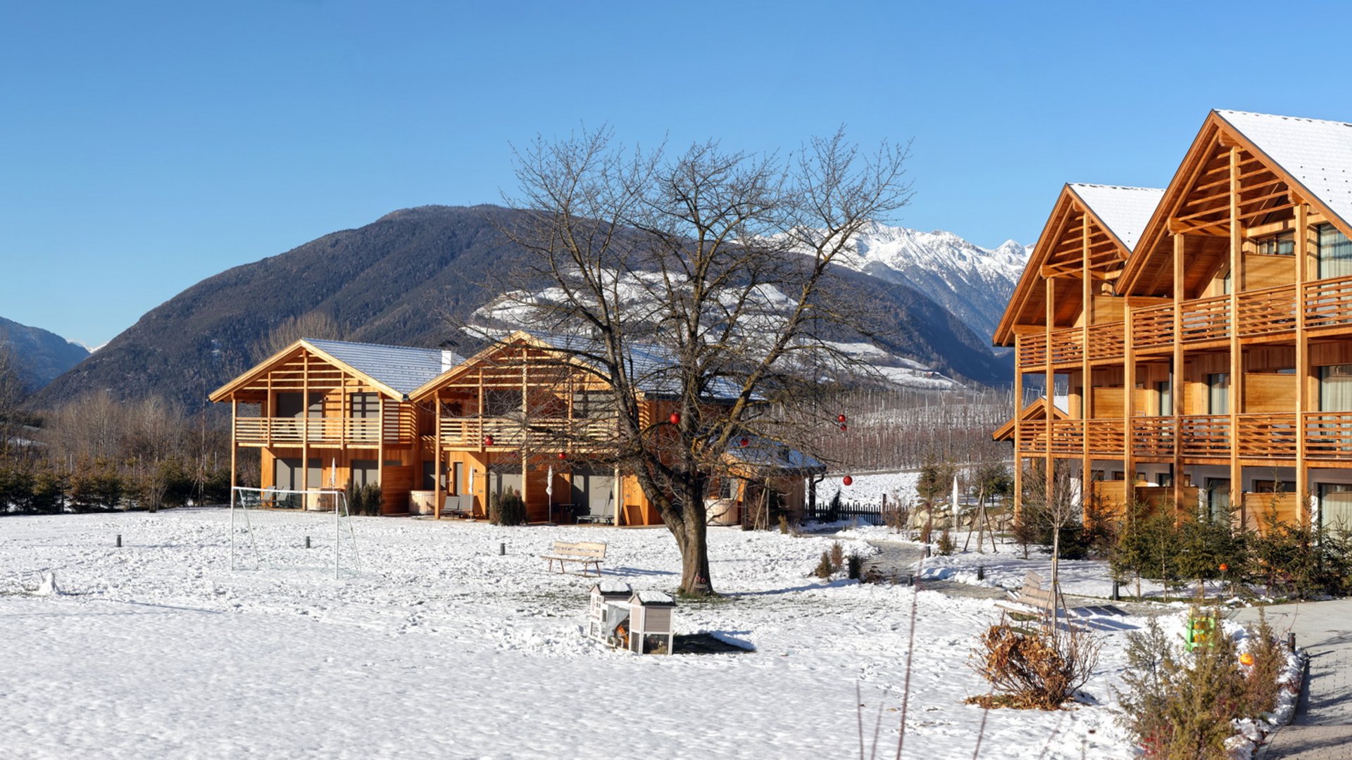 Ferienwohnung in Natz mit dem gewissen Etwas Holzhäuser im Schnee vor Bergen und blauem Himmel