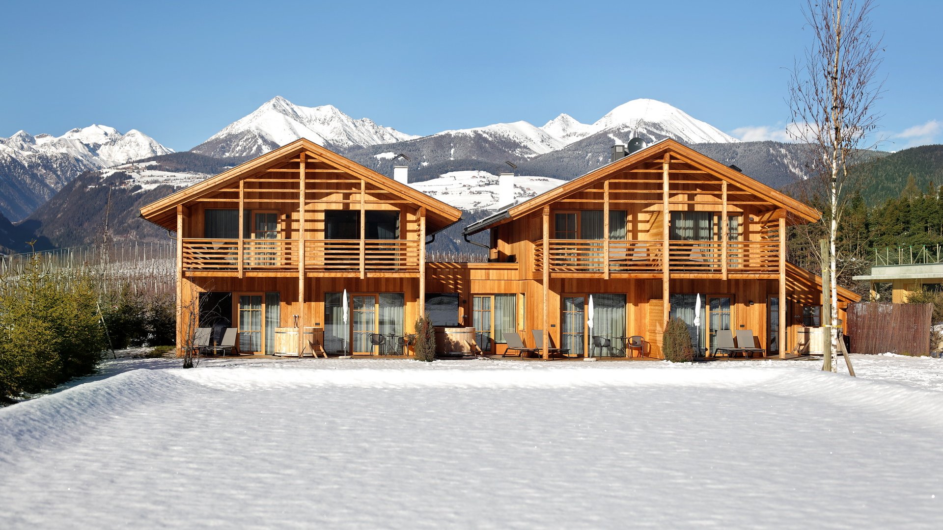 Ferienwohnung in Natz mit dem gewissen Etwas Zwei Holzhäuser mit verschneitem Garten vor verschneiten Bergen