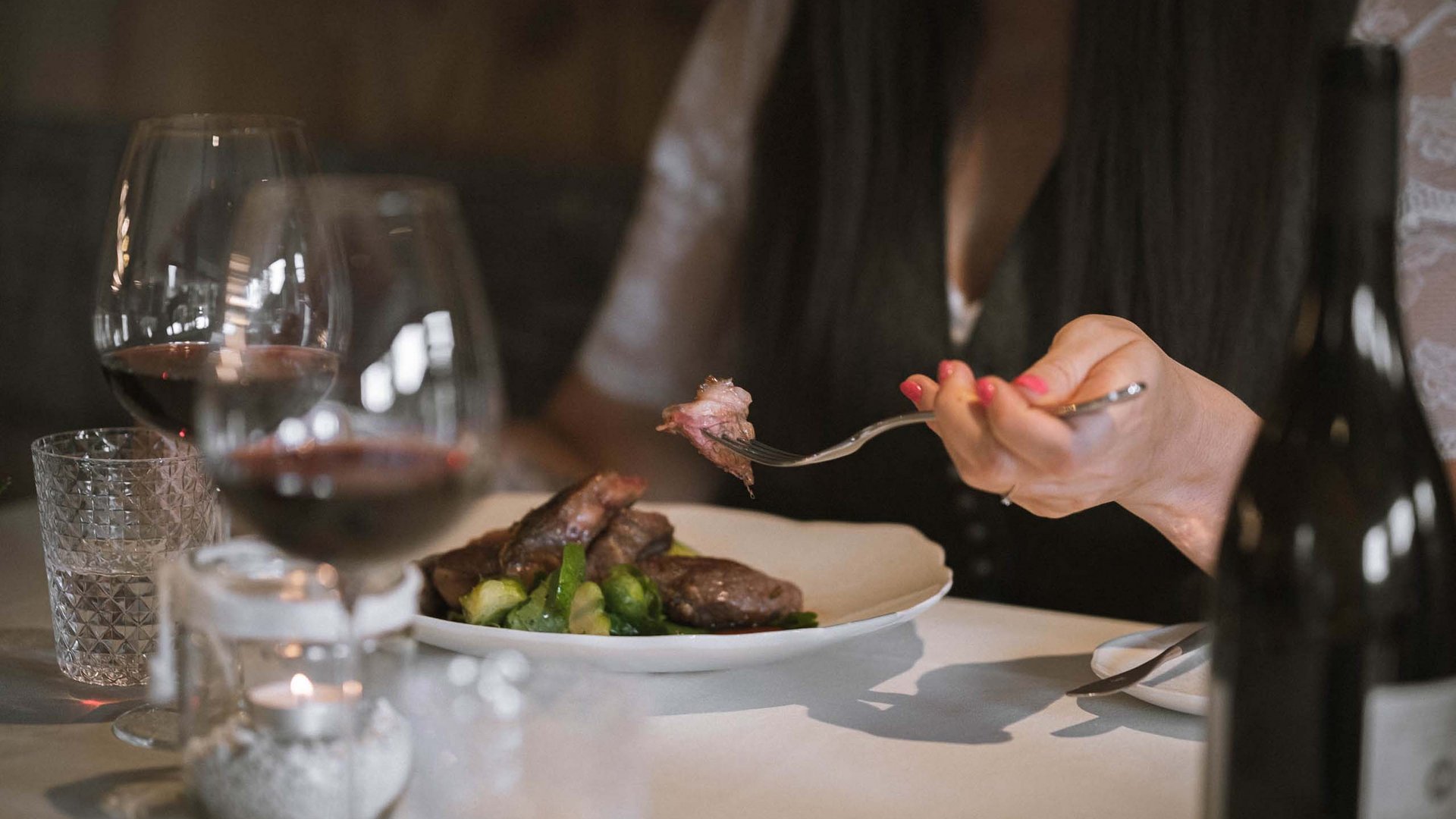 Person isst Steak mit Rosenkohl in elegantem Restaurant mit Rotwein.