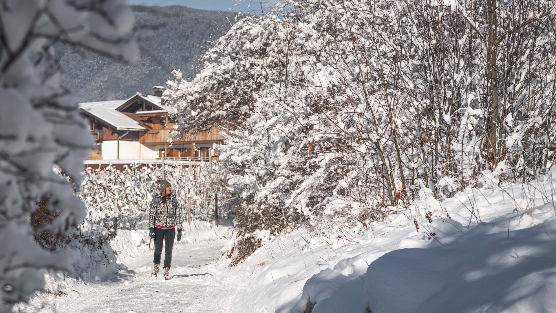 Agriturismo a Bressanone: vacanze invernali Donna che cammina su sentiero innevato vicino ad alberi e case in inverno