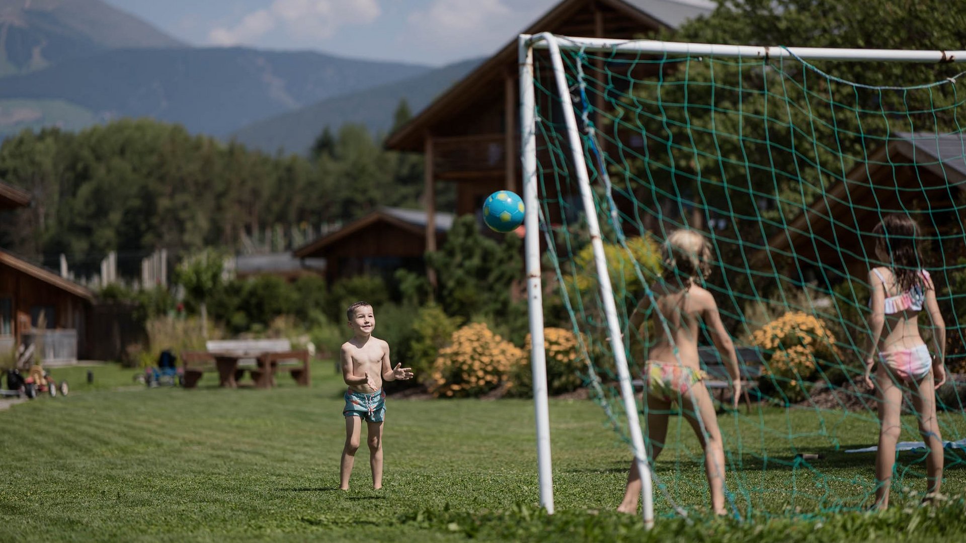 Für Familien Kinder spielen Fußball vor einem Tor auf einer Wiese mit Hütten im Hintergrund