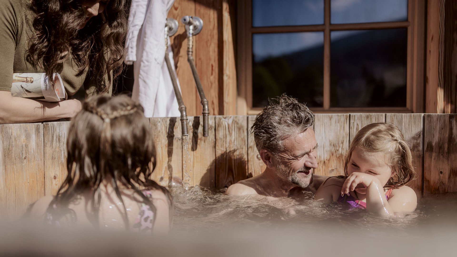 Holiday with a dog in South Tyrol: Kessler’s! Family relaxing together in a wooden tub with bamboo showers outdoors.