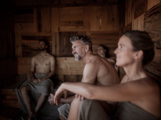 Saunahütte Vier entspannende Menschen sitzen nackt in einer Holzsauna