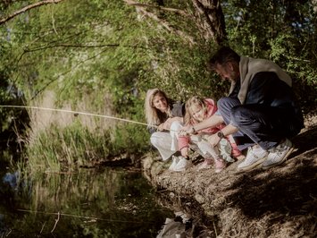 Holiday with a dog in South Tyrol: Kessler’s! Family fishing together by the riverbank in a green natural setting