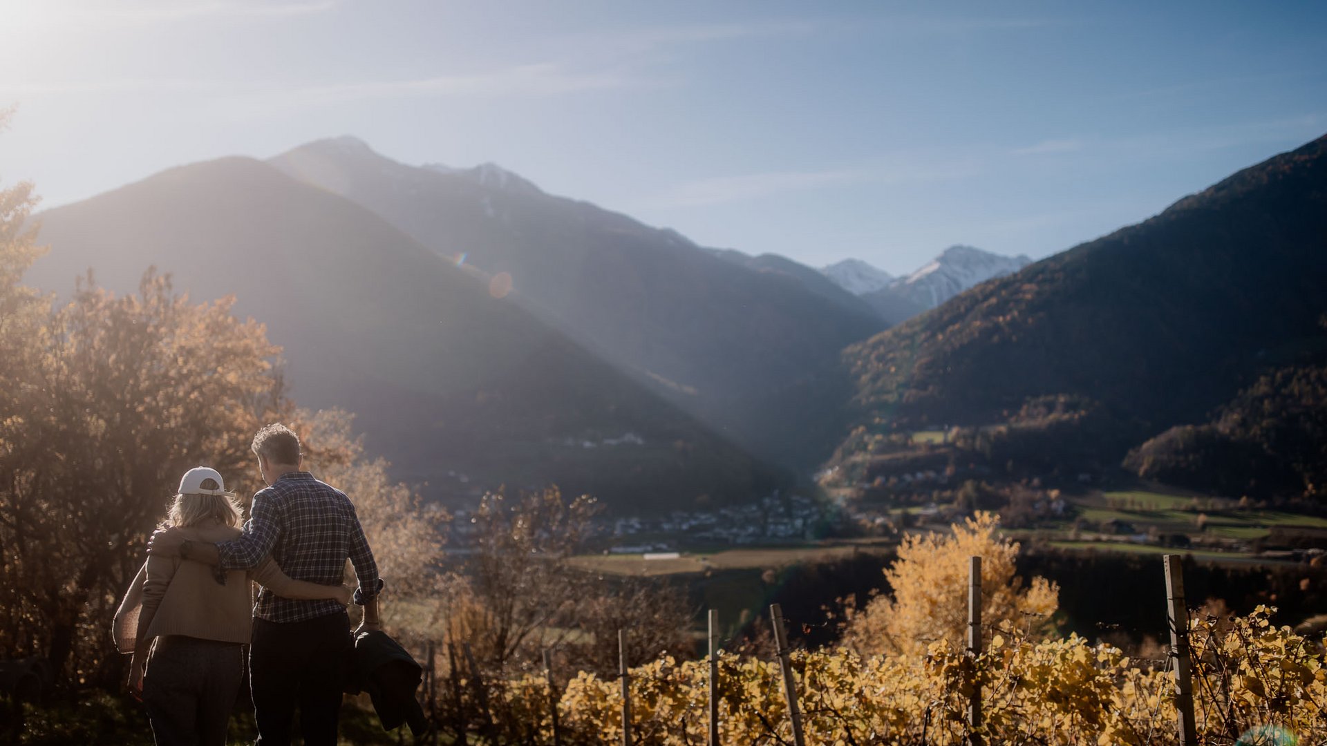 Urlaub nahe Brixen voller Überraschungen Paar umarmt sich im Weinberg mit Bergen und Dorf im Hintergrund bei Sonnenlicht