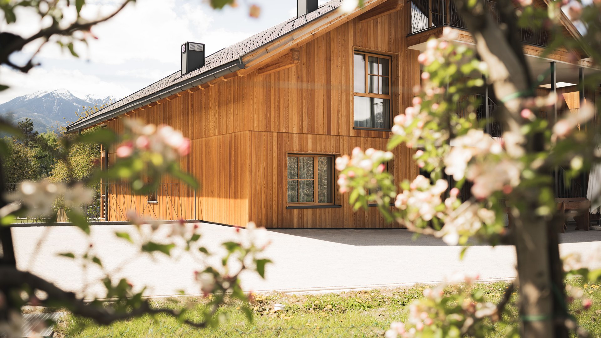 Chalet mit Sauna und noch mehr: Kessler’s Holzhaus mit Bergen im Hintergrund und blühenden Bäumen im Vordergrund