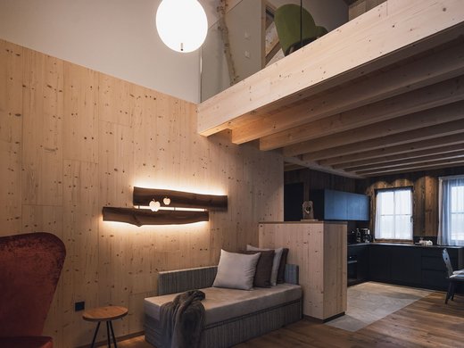 FAQ Living room with wooden walls, cozy sofa, and open kitchen with dining area