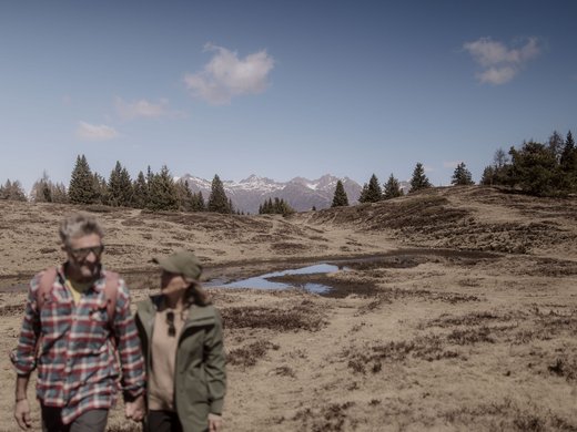 Holiday with a dog in South Tyrol: Kessler’s! Couple hiking in front of mountain landscape with pine trees and clear sky