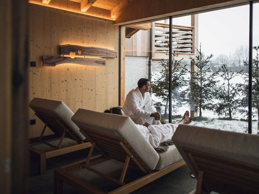 Vacanze in fattoria? Kessler’s Mountain Lodge! Due persone in accappatoio si rilassano su lettini con vista su paesaggio innevato