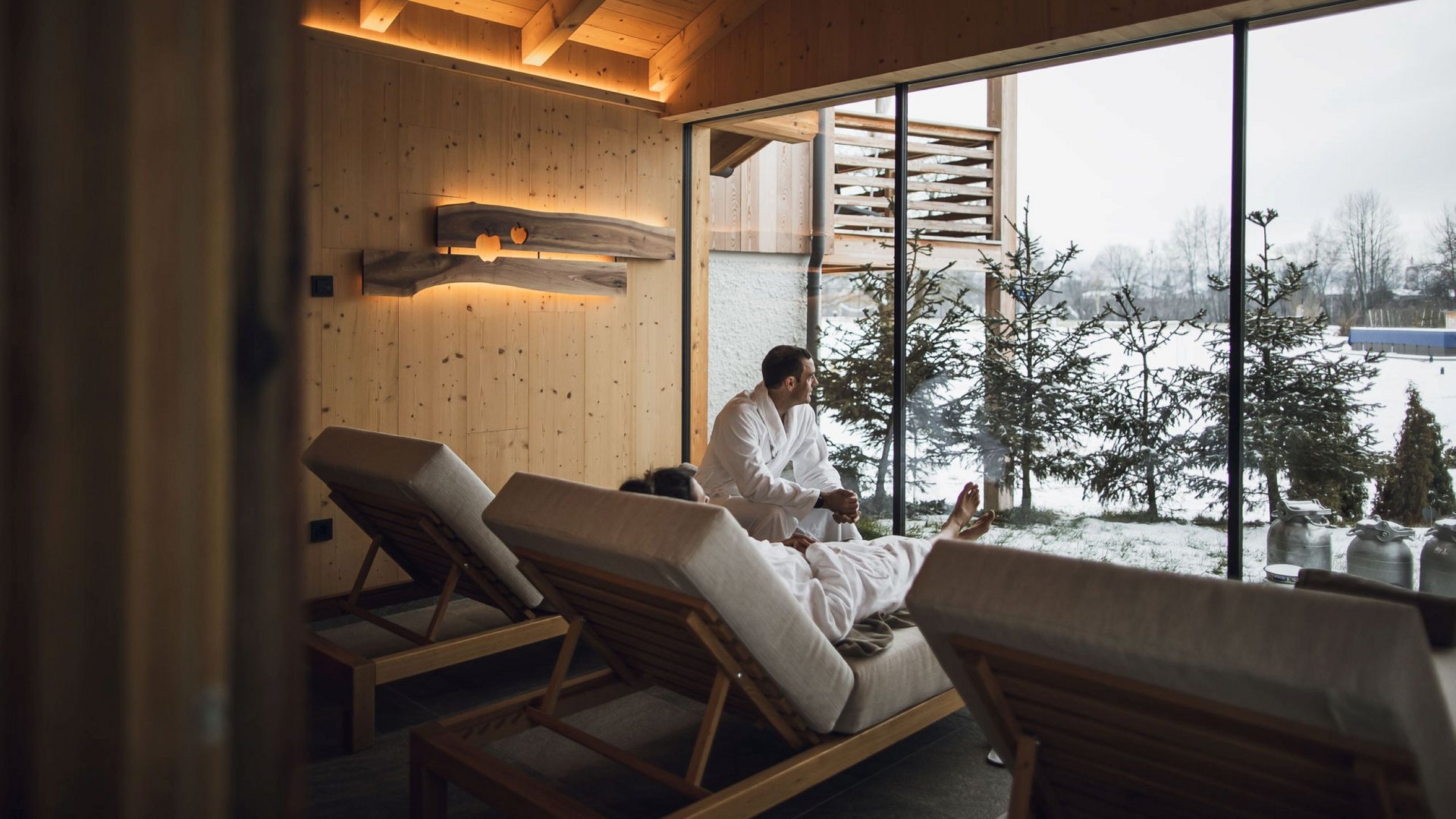 Urlaub in Natz-Schabs? Kessler’s Mountain Lodge! Zwei Personen in Bademänteln entspannen auf Liegen mit Blick auf verschneite Landschaft