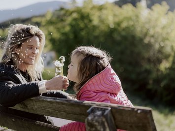 Holiday with a dog in South Tyrol: Kessler’s! Woman and girl playing with dandelions on a bench in a green area