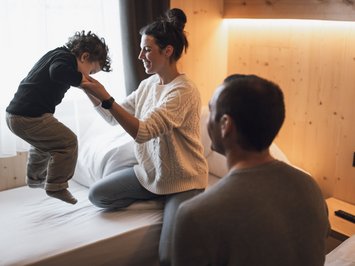 Für Familien Madre tiene il bambino che salta sul letto, padre osserva in una stanza di legno