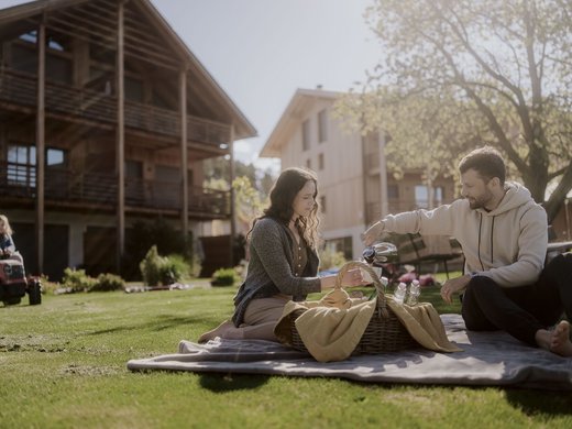 Frisch, regional und so gut. Paar macht Picknick im Garten vor Holzhaus an sonnigem Tag