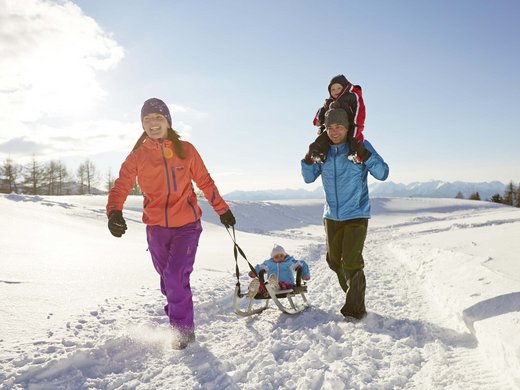 Agriturismo a Bressanone: vacanze invernali Famiglia con bambini che gioca con la slitta sulla neve in una giornata invernale soleggiata