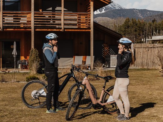 FAQ Two cyclists with helmets standing by bikes in front of a wooden mountain house