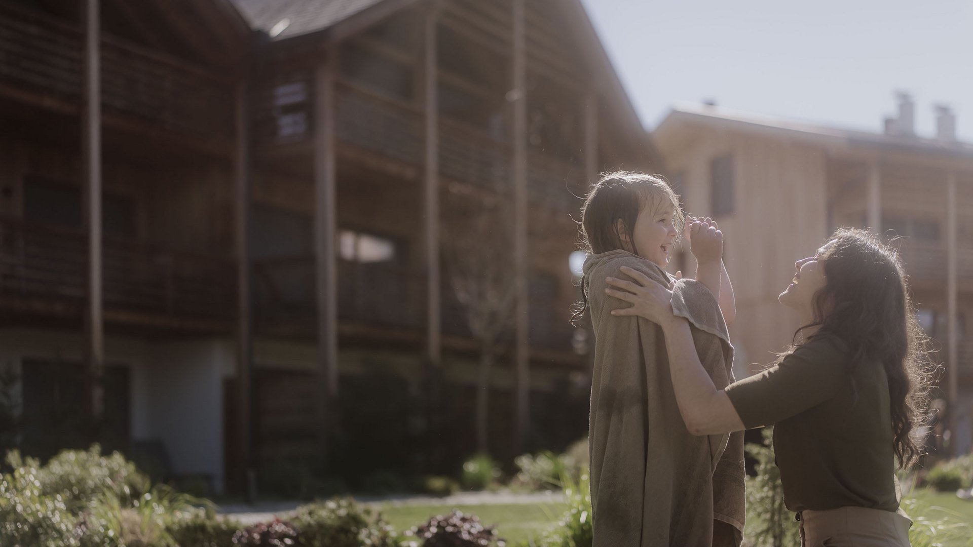Holiday with a dog in South Tyrol: Kessler’s! Mother playing with smiling child outside wooden houses in sunlight
