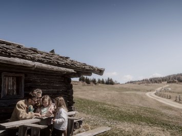 Holiday with a dog in South Tyrol: Kessler’s! Family sitting outside a wooden cabin in rural mountain landscape under clear sky